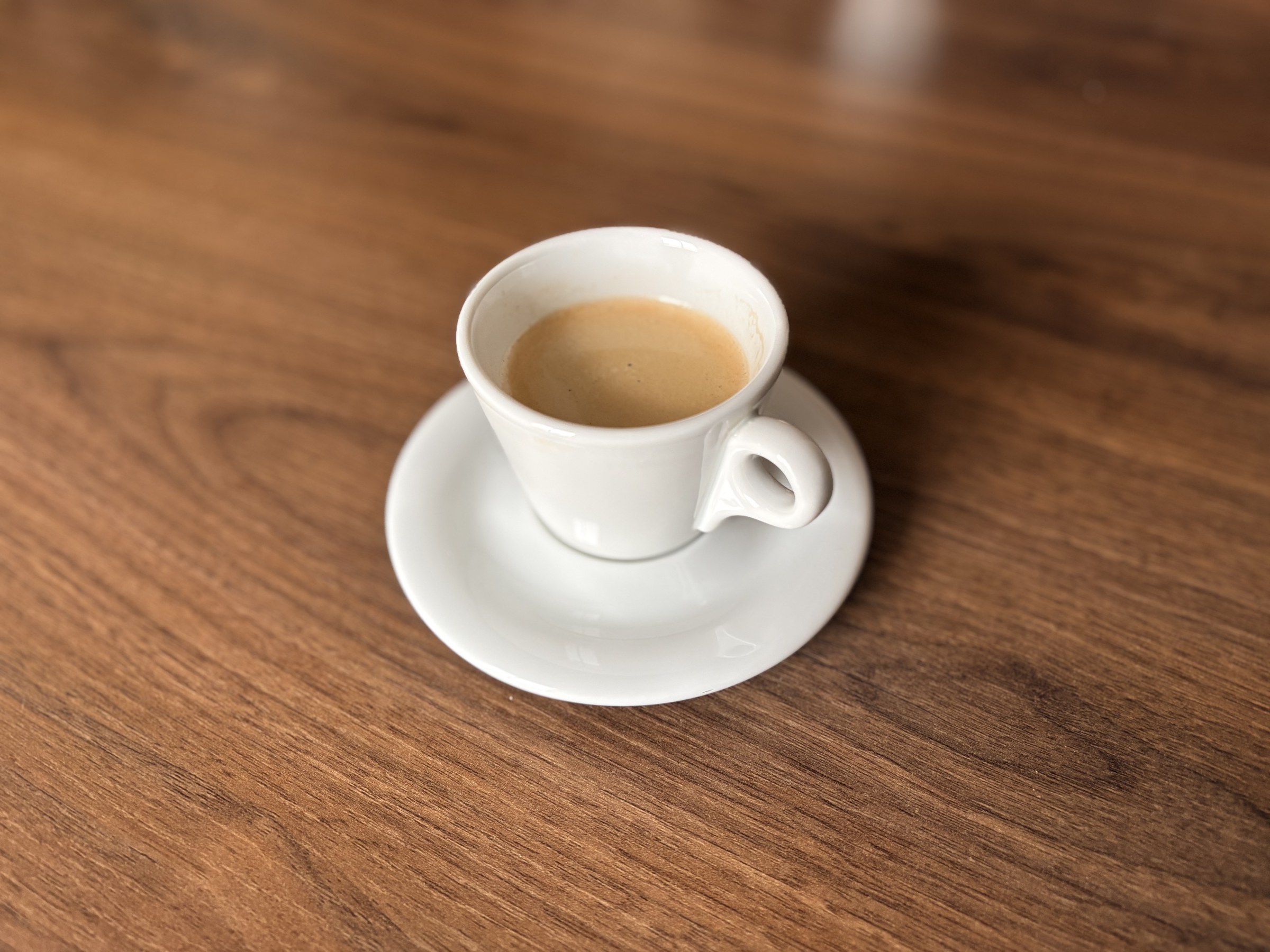 An espresso in a white cup on a walnut table